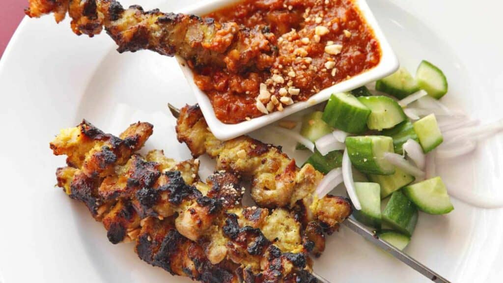 Thai Moo Satay, a popular street food in Thailand, which is pork on a stick, served with sour cucumber and chili sauce