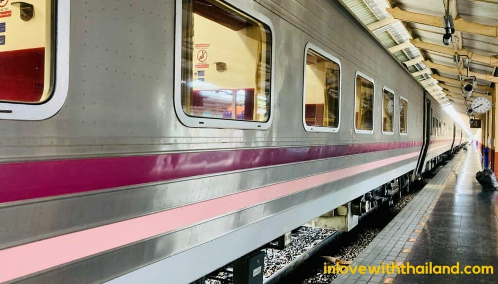 Train standing still at the Bang sue railway station in Bangkok. The train is grey colored with pink and purple stripes.