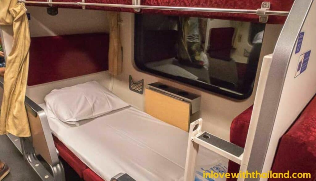 showing a bunk bed inside of a Thailand sleeper train, with white sheets and yellow curtains